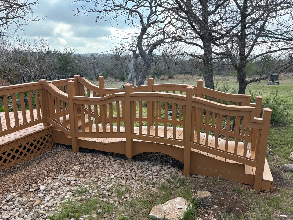 Wood deck with arched, bridge-style railings among Hill Country oaks