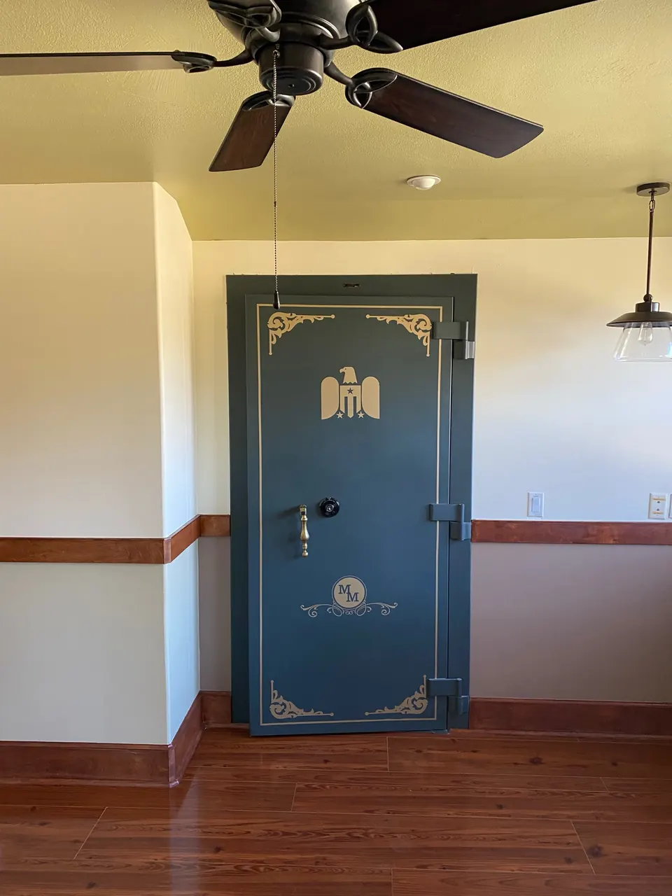 Gun vault door set into a finished room with wood floors and a stained chair rail