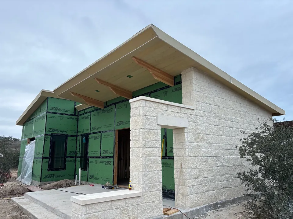 New limestone building going up: cut stone, sheathed walls and a deep roof overhang on wood brackets