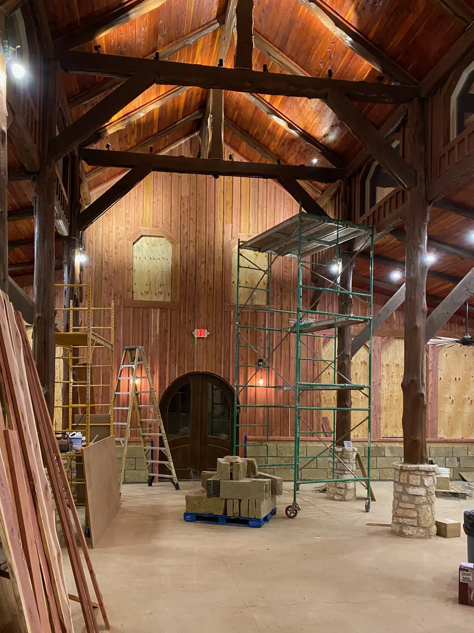 The timber-frame hall under construction: vaulted wood ceiling, log posts on stone bases and scaffolding